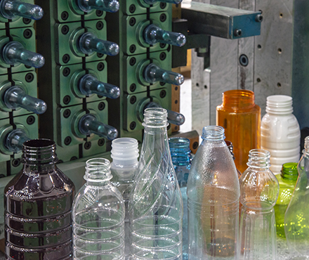 Close-up of PET plastic bottle manufacturing process showing molds and various transparent, colored, and textured plastic bottles.