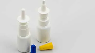 Two white nasal spray bottles, one with a blue cap and one with a yellow cap, against a white background.