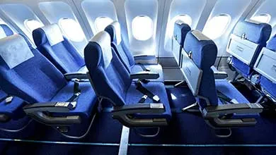 Empty, dark blue airplane seats with orange headrests next to two bright windows.