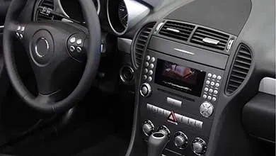 Close-up of a modern car's dark interior, featuring the steering wheel, dashboard, center console, digital screen, and numerous buttons.