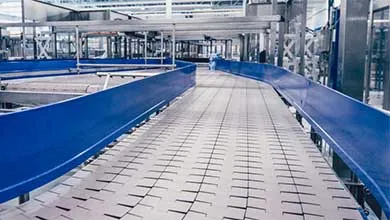 Empty, curving conveyor belt with white segments and blue rails in a factory.