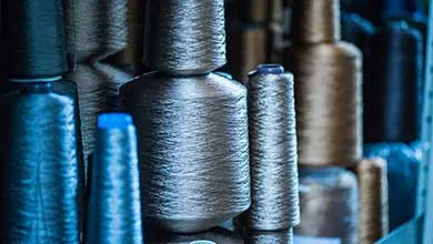 Multiple spools of industrial yarn in neutral and blue tones stacked vertically on shelving.