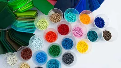 Small clear plastic cups hold colorful round beads—red, blue, green, yellow, pink, orange, white, brown, and black—arranged in rows next to folded fabric swatches in green and blue shades.